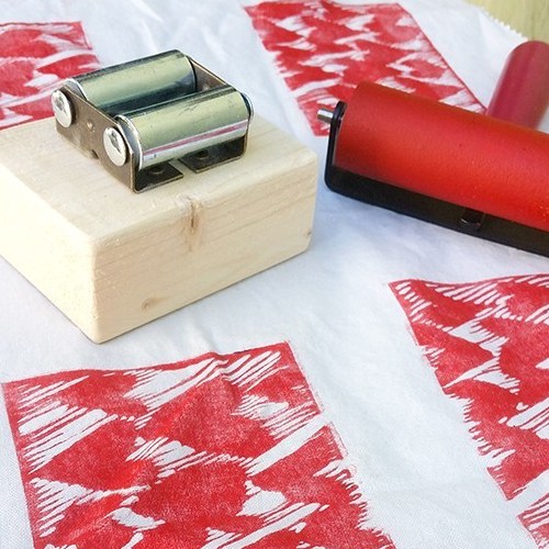 One way to print seamless patterns on kitchent towels. Photo shows printmaking on fabric with a pocket printmaking press and brayer. The fabric blockprint is of many sketchy hearts